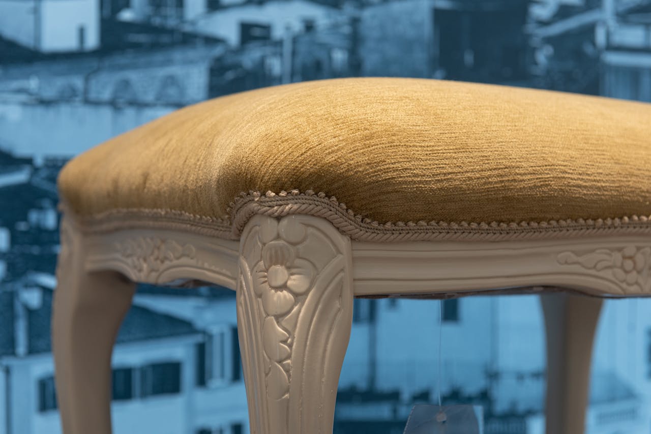 our-experience Close-up of a vintage stool with beige upholstery against a cityscape backdrop.